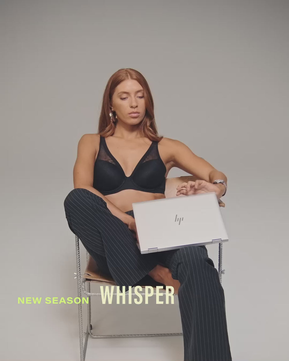 model-poses-on-chair-with-laptio-wearing-black-bra-and-pinstripe-trousers